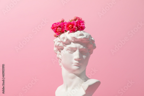 Photography Ancient head with flowers on pink background