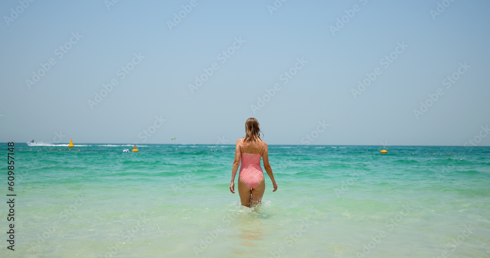 Tourist woman in swimsuit preparing for swimming on Jumeirah beach in Dubai. Tourist woman in swimsuit preparing for swimming on Jumeirah beach in Dubai.