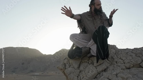 A youthful young shaman in the lotus position prays on a rock against the backdrop of sunset among the sand dunes of the desert photo