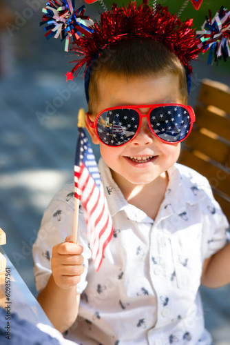 A little boy with a U.S. flag, glasses with a shiny decoration on his head is smiling. A child on a holiday, Independence Day in bright beautiful festive accessories. Happy child with glasses