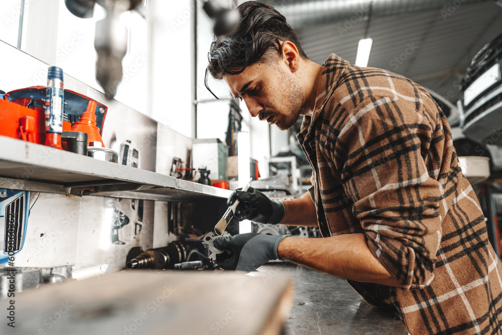 Young man mechanic repairing car parts on worktable in car service shop Young man mechanic repairing car parts on worktable in car service shop