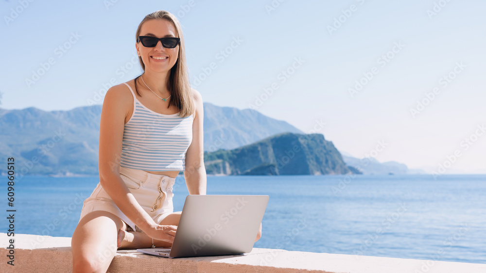 Young woman embraces the freelance lifestyle, effortlessly working on her laptop while appreciating the calming presence of the sea