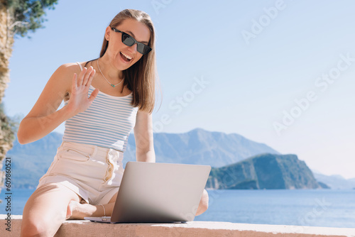 An attractive woman during a video call with friends during a vacation. Sea and mountains on the background