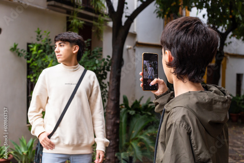Younger brother takes a picture of older brother in a garden with houses and trees in the background
