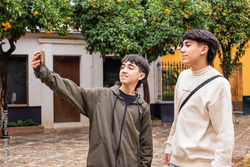 younger brother and older brother take a selfie on the streets of Seville, Spain. In the background there are orange trees