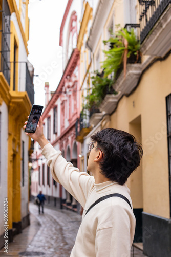 twenty-year-old boy with glasses and brown hair, takes a selfie during a walk in the streets of Seville, Spain