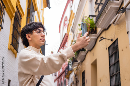 twenty-year-old boy with glasses and brown hair, takes a picture with his cell phone of the streets of the center of Seville, Spain