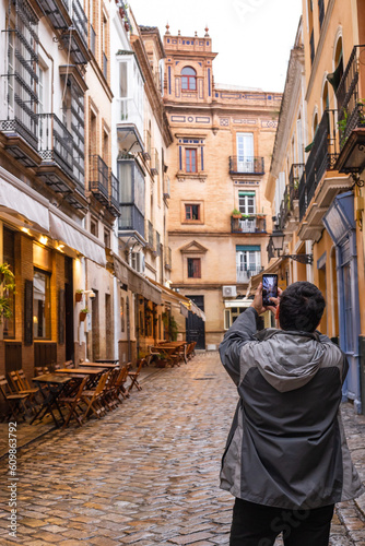 50-year-old man, taking a picture with his cell phone of a street, walking around in the center of Seville, Spain