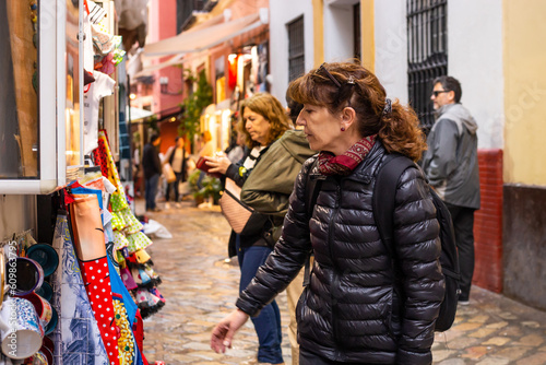 Fifty-year-old woman walks with her family through the native shops of Seville, Spain. She is looking at some cups and flamenco-style dresses