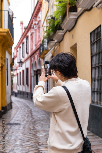 twenty-year-old boy with glasses and brown hair, takes a picture with his cell phone of the streets of the center of Seville, Spain