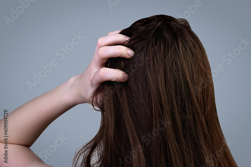 A young woman with dirty greasy hair on a gray background. photo