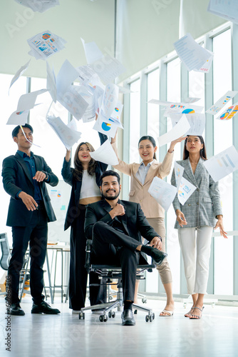 Vertical image of Asian business man and woman throw several paper up over the manager sit on chair and look at camera with confidence to show successful of the project.