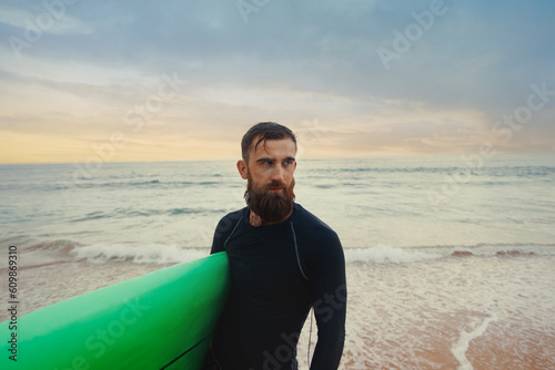 Young bearded man with surfboard standing near a beach. Man with surfing board outdoors on a summer day.