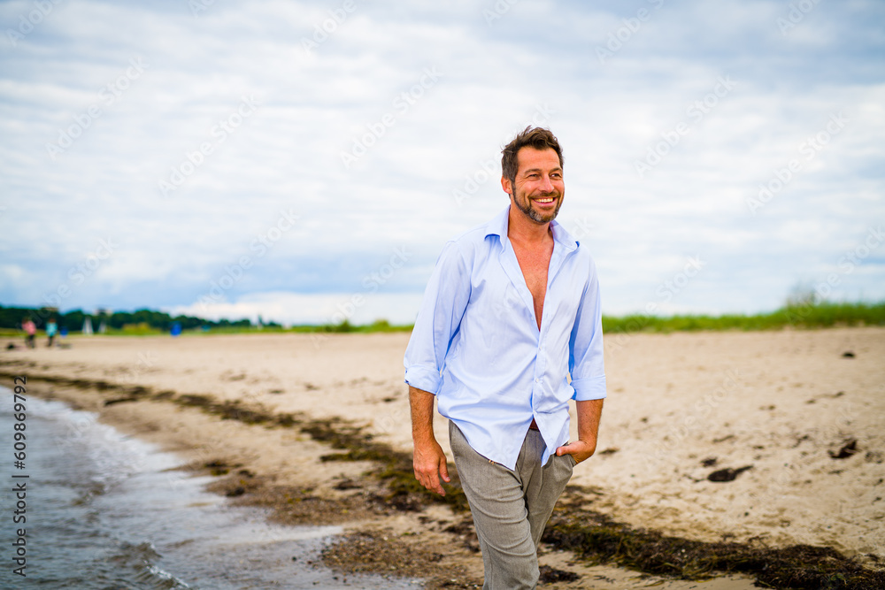 Handsome middle-aged man walking on the beach in summer Handsome middle-aged man walking on the beach in summer