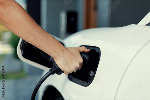 Progressive concept of hand insert an emission-free power connector to the battery of electric vehicle at home. Electric vehicle charging via cable from charging station to EV car battery