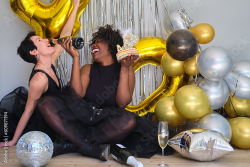 Canvas Print Two multiracial women in a 40 birthday party laughing drinking champagne from bottle