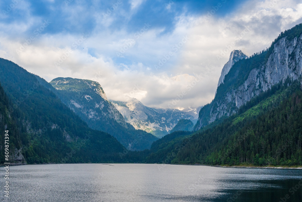 Beautiful landscape mountain forest lake view. Amazing summer cloudy scenery of Gosausee mountain lake and Dachstein mountain summit. Colorful scenery in Alps. Popular travel and hiking destination.