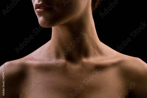 Bust of a woman, focusing on the neck and shoulders, frontal view, natural skin, lighting with shadows, definition of the collarbones and neck muscles, natural model on black background