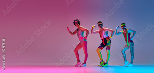 Fototapeta Naklejka Na Ścianę i Meble -  Three men in colorful retro sportswear training, doing aerobics exercises against gradient blue pink background. Concept of sportive and active lifestyle, humor, retro style. Banner. Copy space for ad