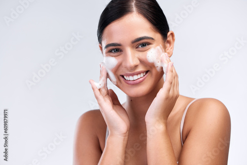 Beauty, foam wash and portrait of a woman in a studio for natural, cosmetic and skincare routine. Wellness, smile and female model cleaning her face with facial cleanser isolated by white background photo