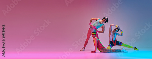 фотографія Flexible men in colorful, vintage sportswear stretching against gradient blue pink studio background in neon light