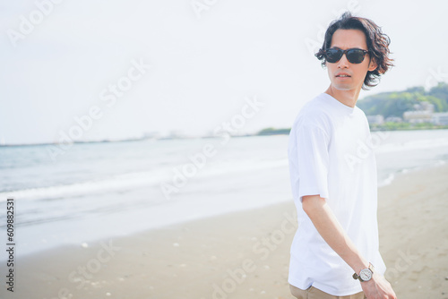 Fototapeta Naklejka Na Ścianę i Meble -  夏の海岸を歩くサングラスをかけた男性