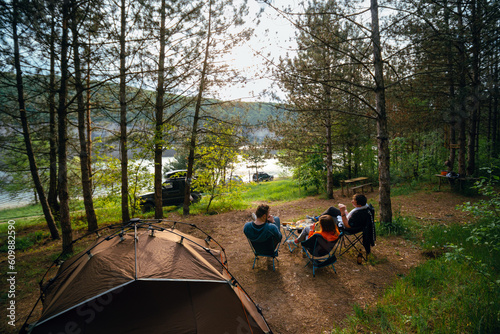Happy campers. Rearview shot of tThree friends are relaxing with a view of the river. spending time in nature. Quick folding tent equipment, lightweight chairs. Good mood. SUV off road vehicles