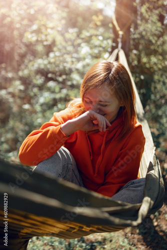 Portrait of a woman, a girl sits in a hammock and laughs, has a good mood. Coniferous forest, rest of the wild nature. Vertical photo