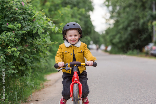 Fototapeta Naklejka Na Ścianę i Meble -  A cheerful little boy rides a running bike in a helmet outdoors. A happy child is engaged in an active sport. Protection. Life insurance and child safety.