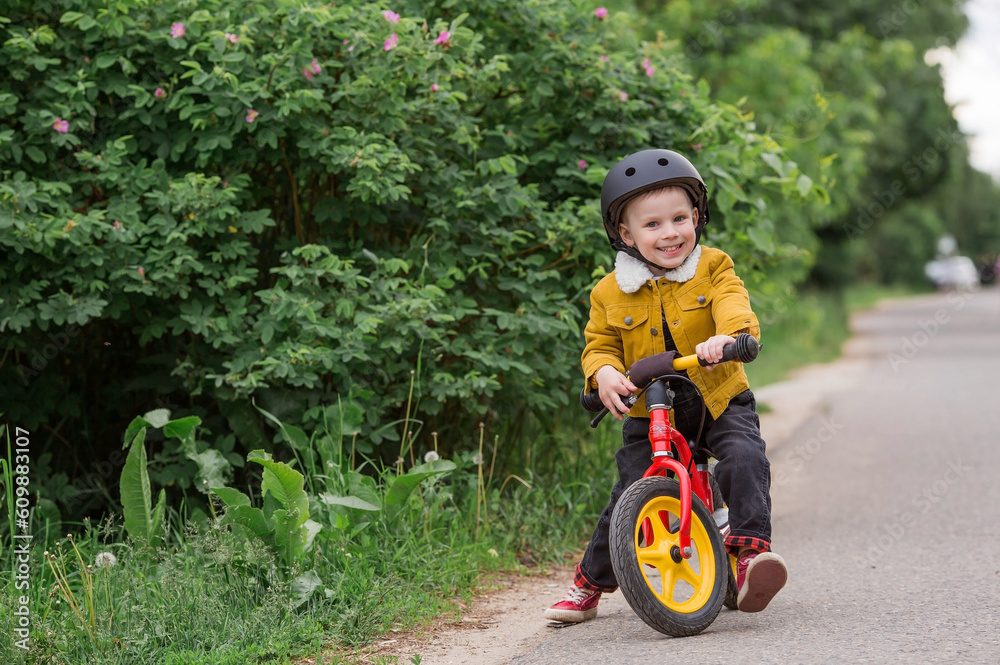 A cheerful little boy rides a running bike in a helmet outdoors. A happy child is engaged in an active sport. Protection. Life insurance and child safety. A cheerful little boy rides a running bike in a helmet outdoors. A happy child is engaged in an active sport. Protection. Life insurance and child safety.