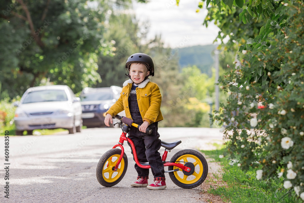 A cheerful little boy rides a running bike in a helmet outdoors. A happy child is engaged in an active sport. Protection. Life insurance and child safety. A cheerful little boy rides a running bike in a helmet outdoors. A happy child is engaged in an active sport. Protection. Life insurance and child safety.