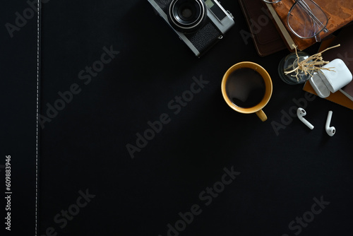 Stylish workplace with retro camera, coffee cup, earphones and glasses on black surface. Top view with copy space for your text