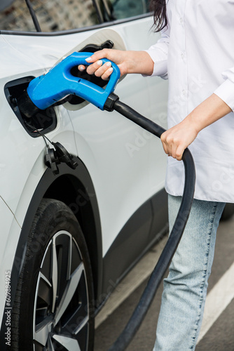 Young business woman refueling her electric car at a EV charging station. Concept of environmentally friendly vehicle. Electric car concept. Green travelling.