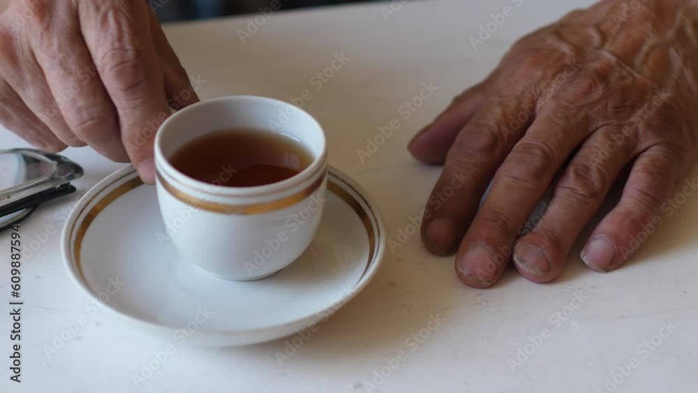 a pensioner sitting at a table drinks tea from a cup from a saucer, reading glasses are nearby on the table. traditional breakfast, lifestyle of an older person a pensioner sitting at a table drinks tea from a cup from a saucer, reading glasses are nearby on the table. traditional breakfast, lifestyle of an older person