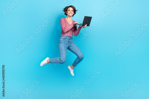 Full length portrait of energetic pretty person jumping use netbook isolated on blue color background © deagreez