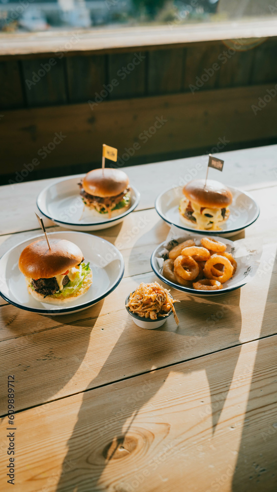 a wooden table topped with plates of snacks, burger, fries. a wooden table topped with plates of snacks, burger, fries.