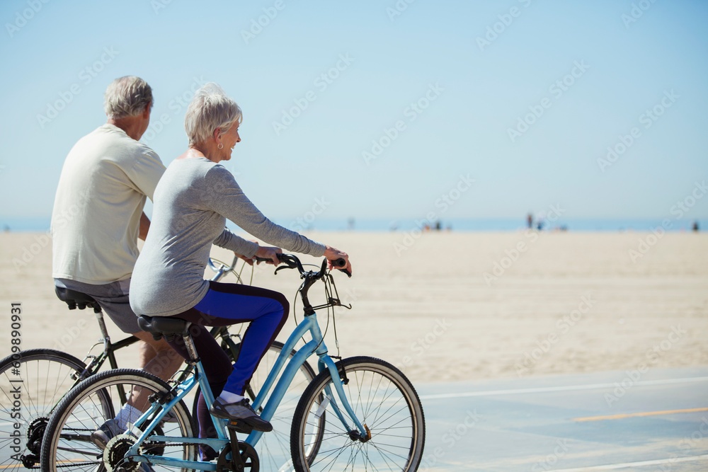 Senior couple riding bicycles on beach - obrazy, fototapety, plakaty 