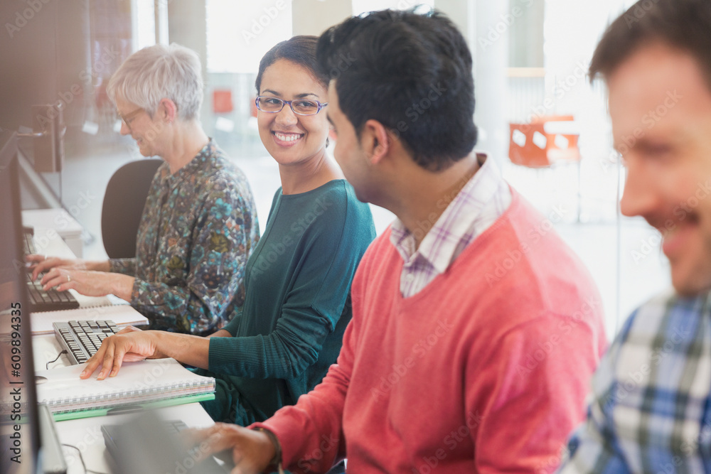 Fototapeta premium Smiling students talking at computers in adult education classroom