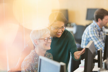 Smiling women talking at computer in adult education classroom