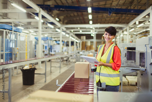 Portrait smiling worker checking cardboard boxes on conveyor belt production line in factory photo