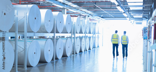 Workers in reflective clothing walking along large paper spools in printing plant photo