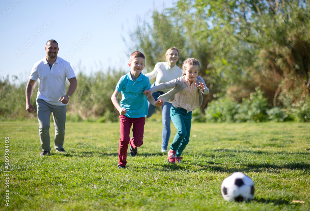 Father with mother with two children enjoy playing soccer on lawn in summer park Father with mother with two children enjoy playing soccer on lawn in summer park