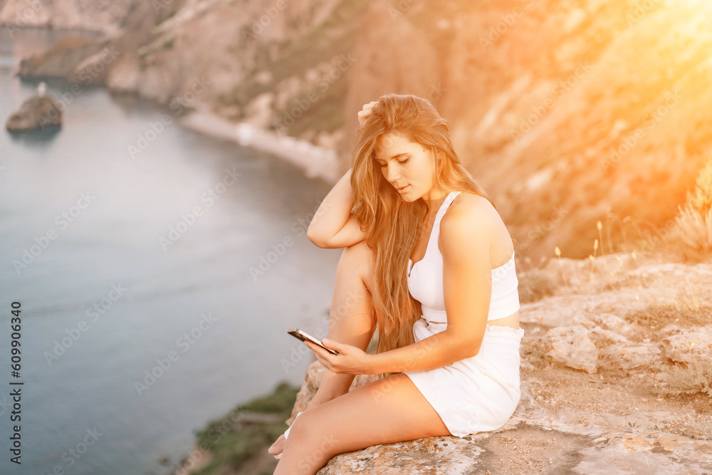 Happy woman in white shorts and T-shirt, with long hair, talking on the phone while enjoying the scenic view of the sea in the background. Happy woman in white shorts and T-shirt, with long hair, talking on the phone while enjoying the scenic view of the sea in the background.