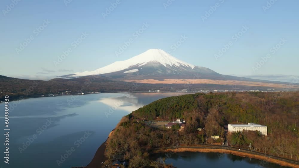 Cinematic aerial of lake yamanaka with mount Fujiyama, snow covered peak in distance. Forest, trees and houses around water. Drone flying forward, golden hour clear warm evening sun light, blue sky. Cinematic aerial of lake yamanaka with mount Fujiyama, snow covered peak in distance. Forest, trees and houses around water. Drone flying forward, golden hour clear warm evening sun light, blue sky.