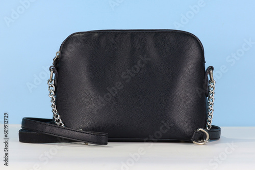 Black female leather bag with shoulder strap on blue background photo