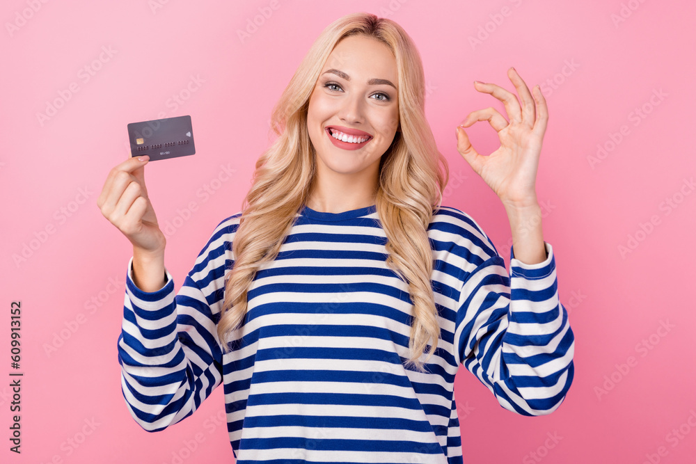 Photo of young financier girl wear pullover show okey symbol plastic debit card enjoy wireless payment isolated on pink color background