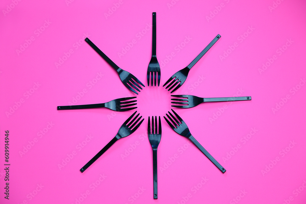 Top view composition of black plastic forks placed on pink background Top view composition of black plastic forks placed on pink background
