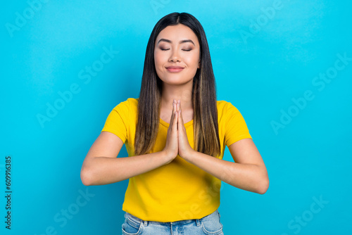 Photo of young korean girl wear yellow trendy t-shirt closed eyes comfort hands together concentration isolated on blue color background