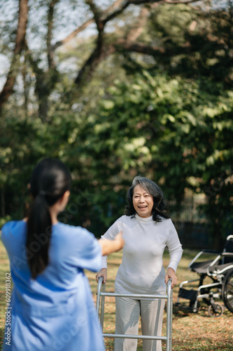 Asian careful caregiver or nurse and the happy patient in a wheelchair are walking in the garden to help and encourage and rest your mind with green nature. Help support yourself 