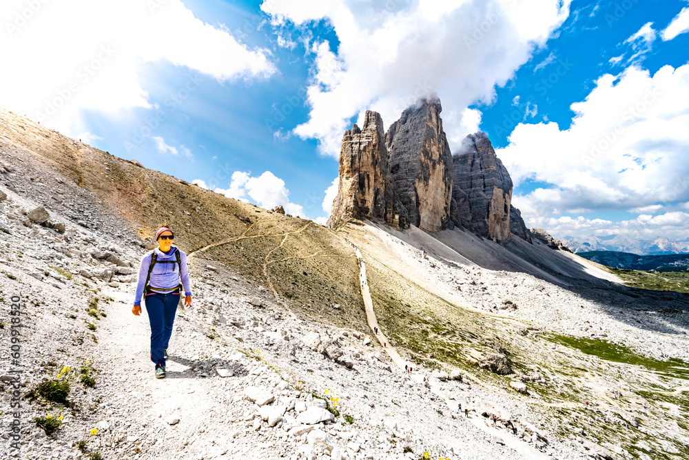 Young athletic woman walks on hike trail at Tre Cime mountain in the morning. Tre Cime, Dolomites, South Tirol, Italy, Europe.